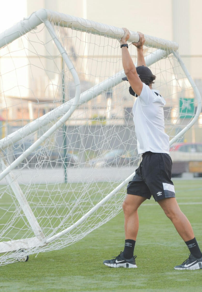 Football (soccer) coach pushing mobile goal — behind-the-scenes leadership and commitment