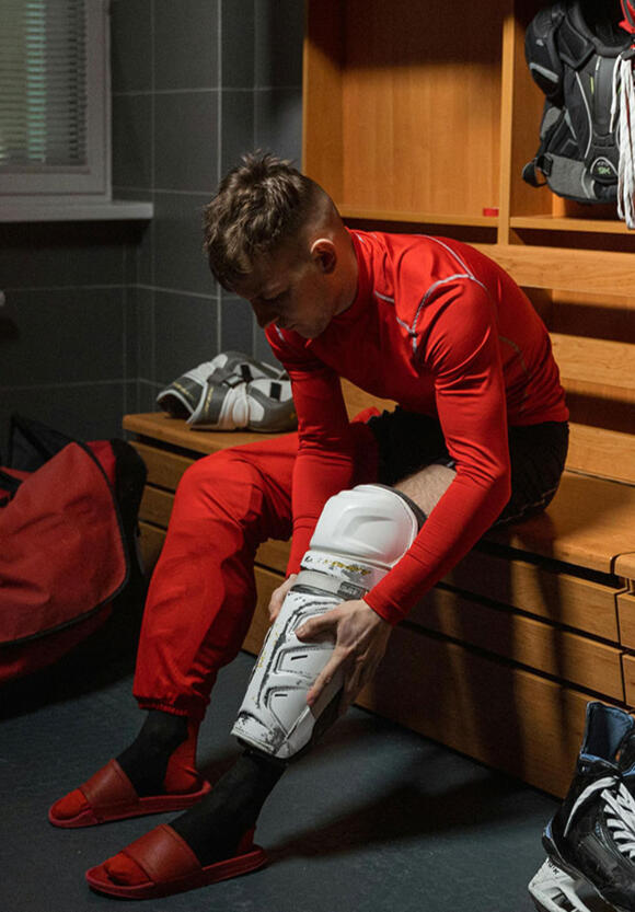 Ice hockey player in locker room putting on shin guards — preparation, ritual, and mindset before the game